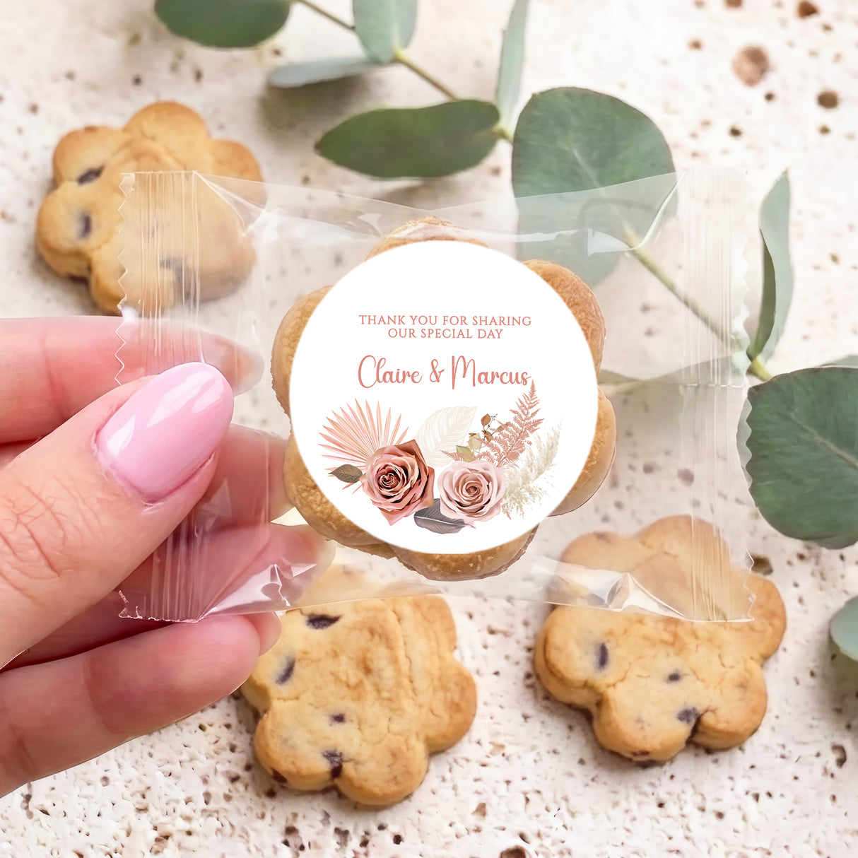 Packaged bite-size cookies with round floral thank-you sticker and pink-nail hand holding