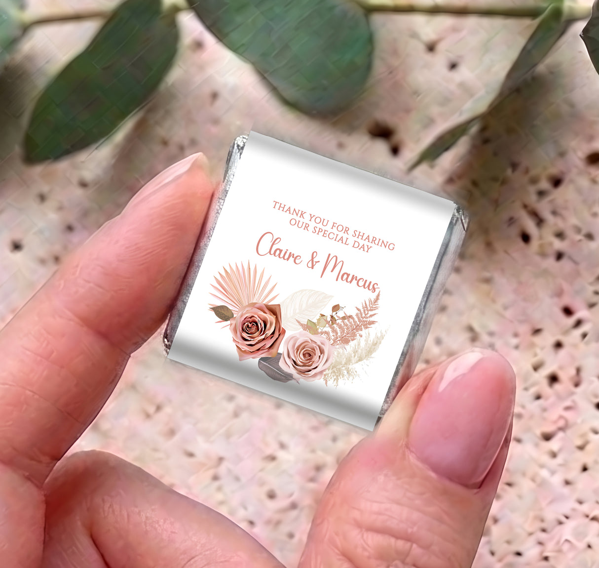 Mini personalised chocolate wrapper with pink rose floral design and names, held in hand.