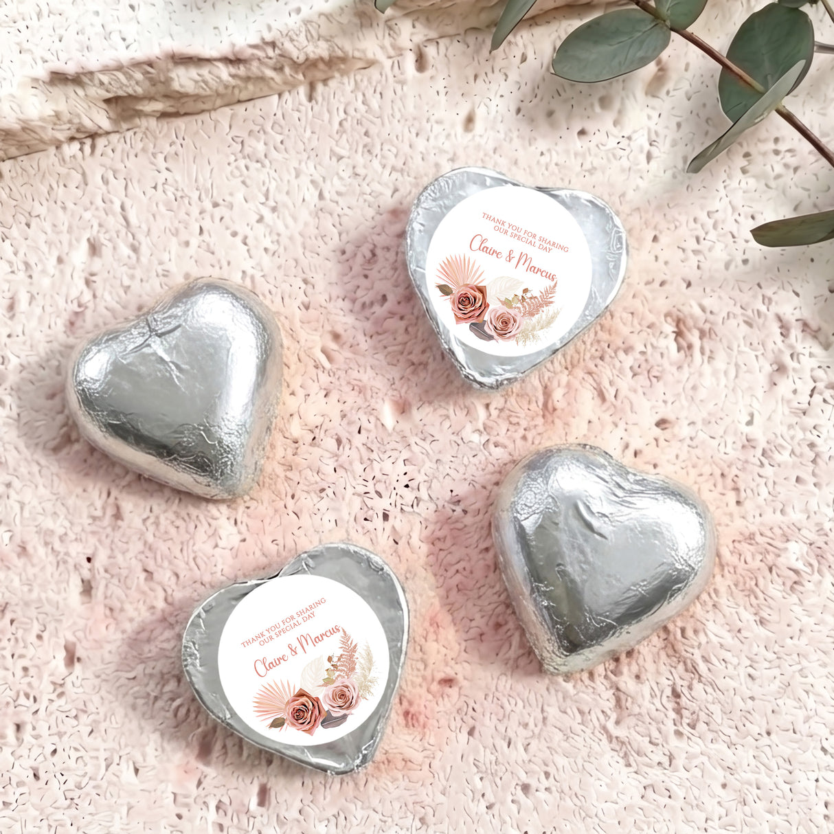 Silver foil-covered chocolate hearts with floral name labels on textured surface