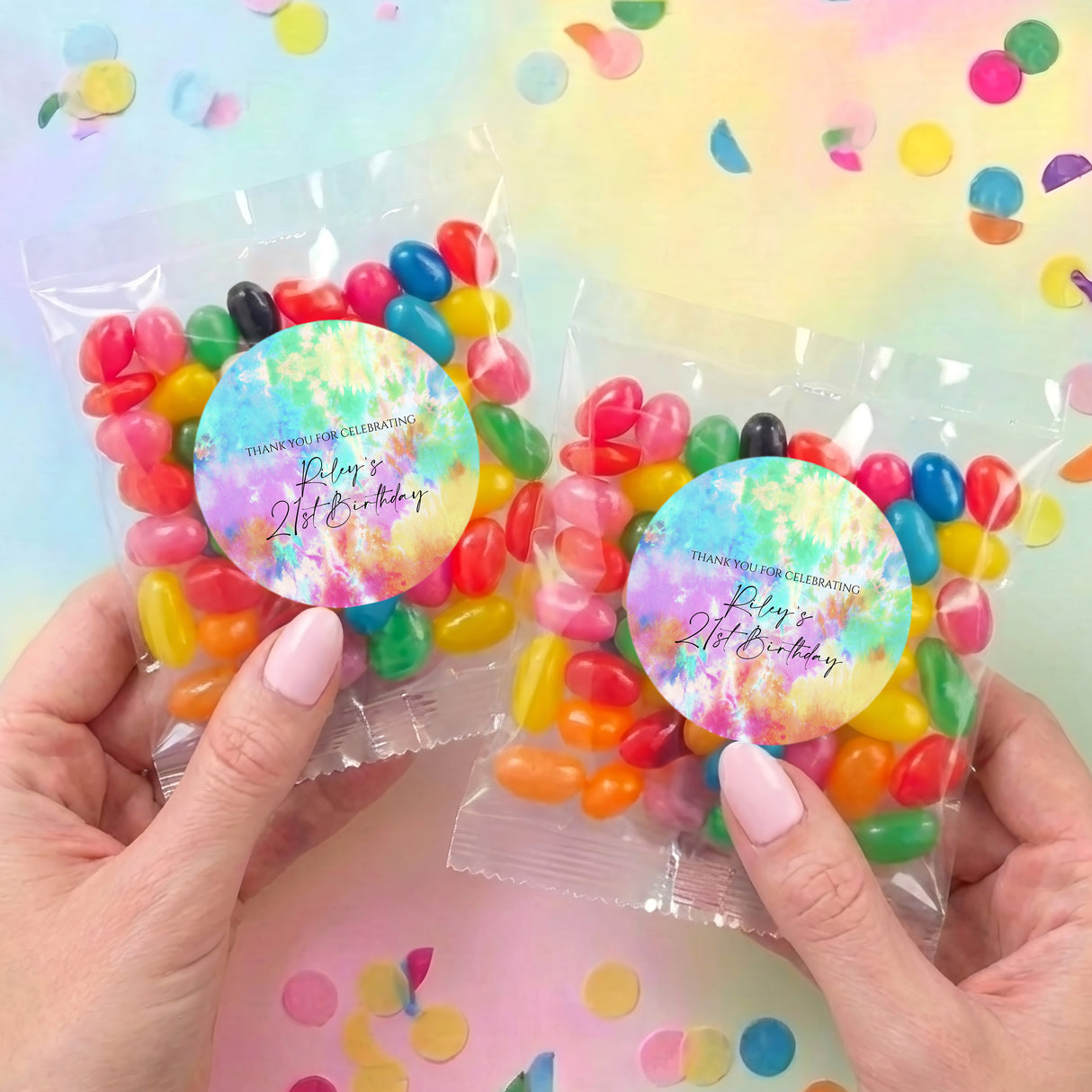 Two personalised tie-dye jelly bean bags held with multicolor candies and round birthday labels