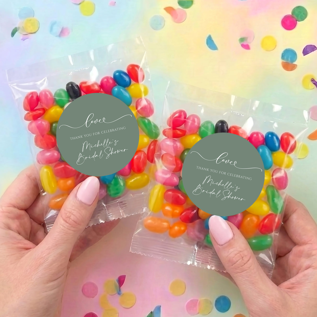 Two clear jelly bean favor bags with colorful beans and sage green 'Love' round labels