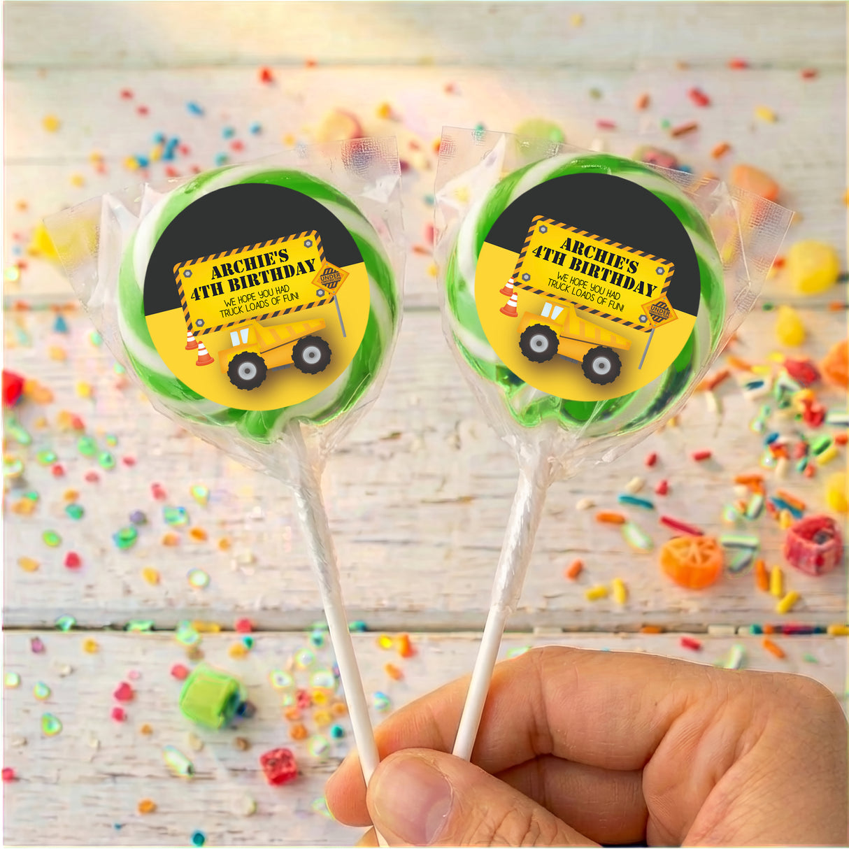 Personalised birthday lollipops with yellow truck labels in green border, held in hand