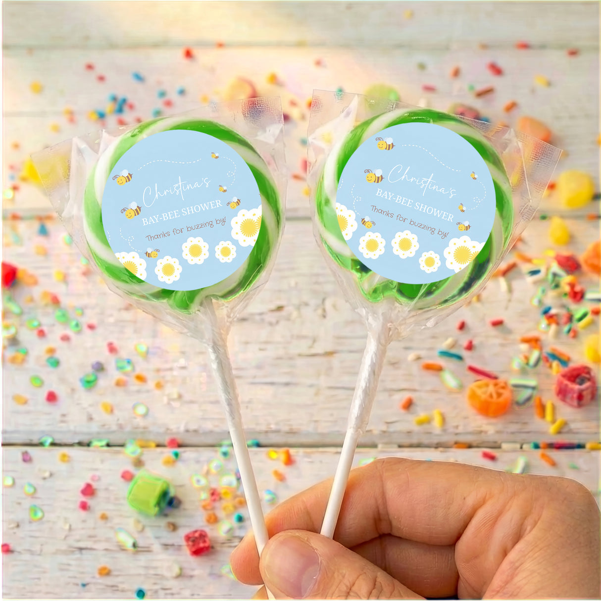 Personalised green bee baby shower lollipops with round blue labels, two wrapped lollipops