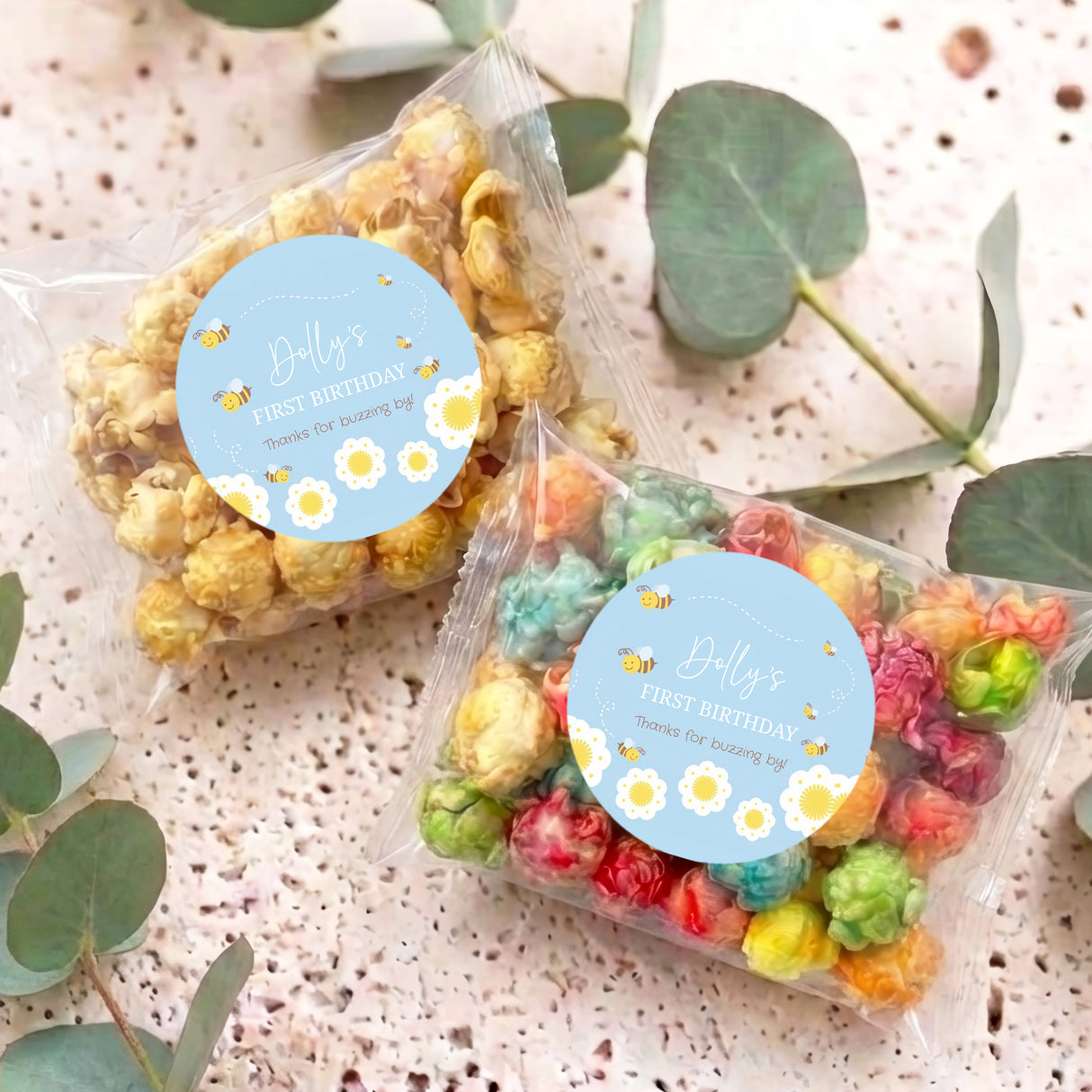 Personalised popcorn bags with blue bee first birthday labels, tied with clear cellophane