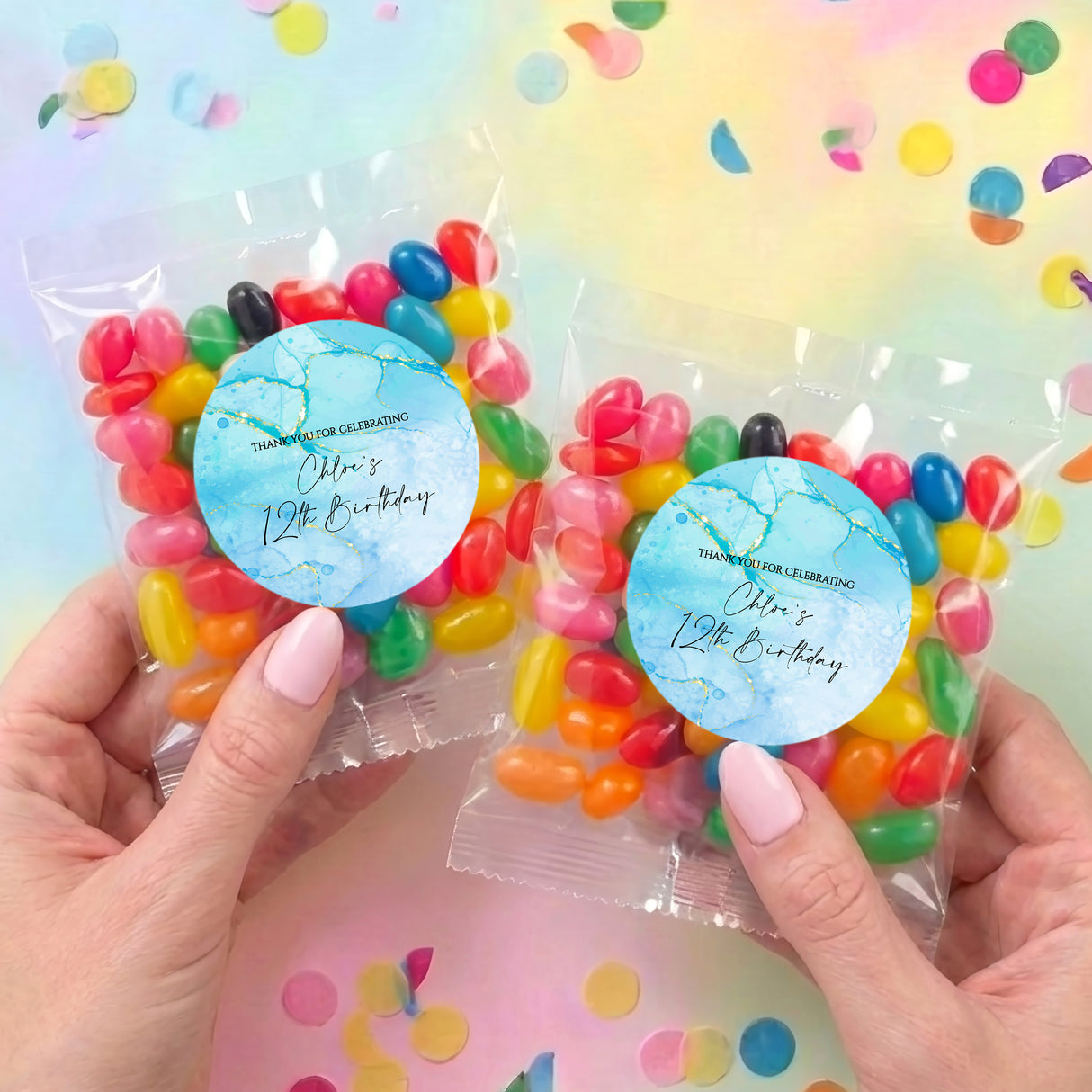 Two personalised jelly bean pouches with blue labels and multicolored candies held by hands