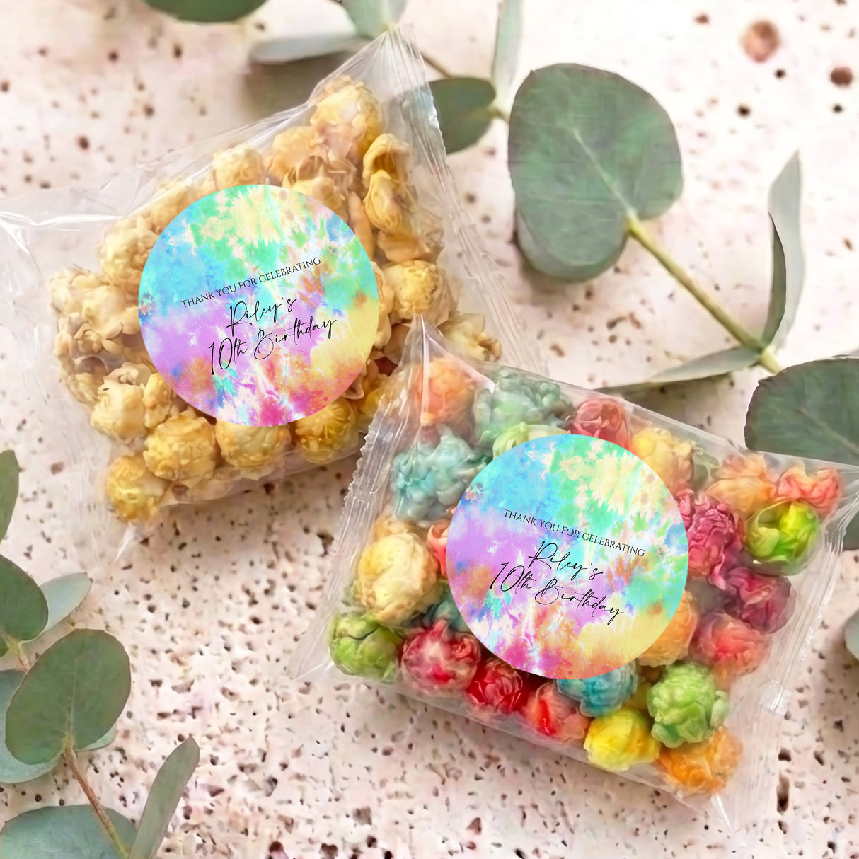 Two kids tie-dye birthday popcorn bags with circular rainbow stickers on display