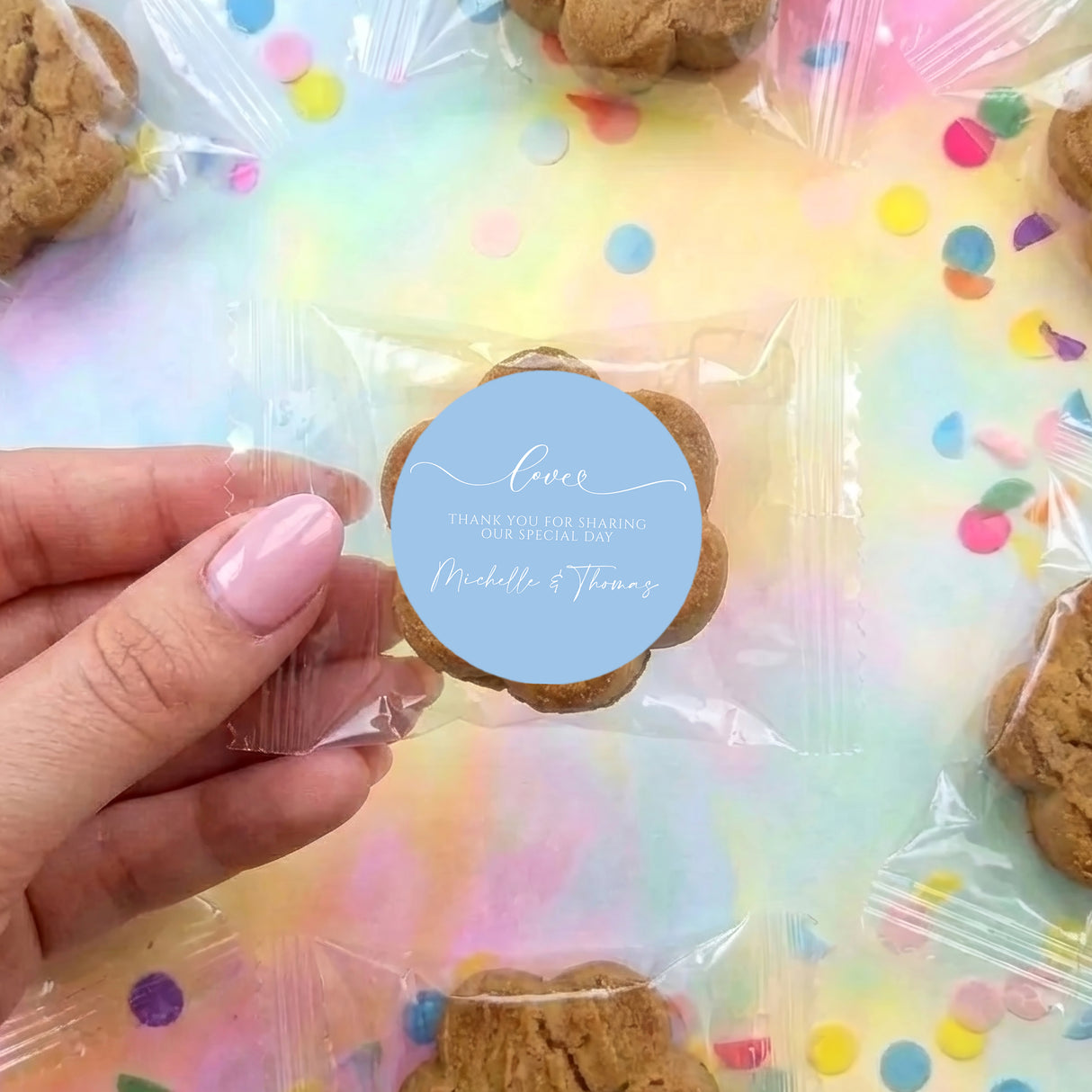 Hand holding bite-size chocolate chip cookie in clear bag with round blue label