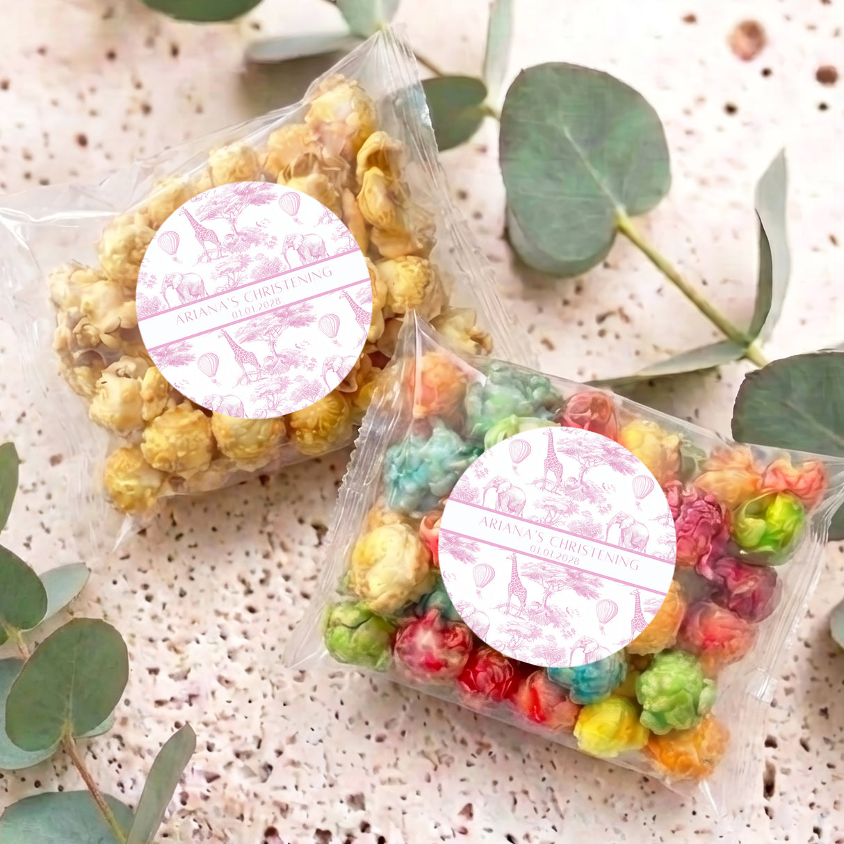 Pink safari-themed popcorn bags with round white personalised labels, lying on speckled surface