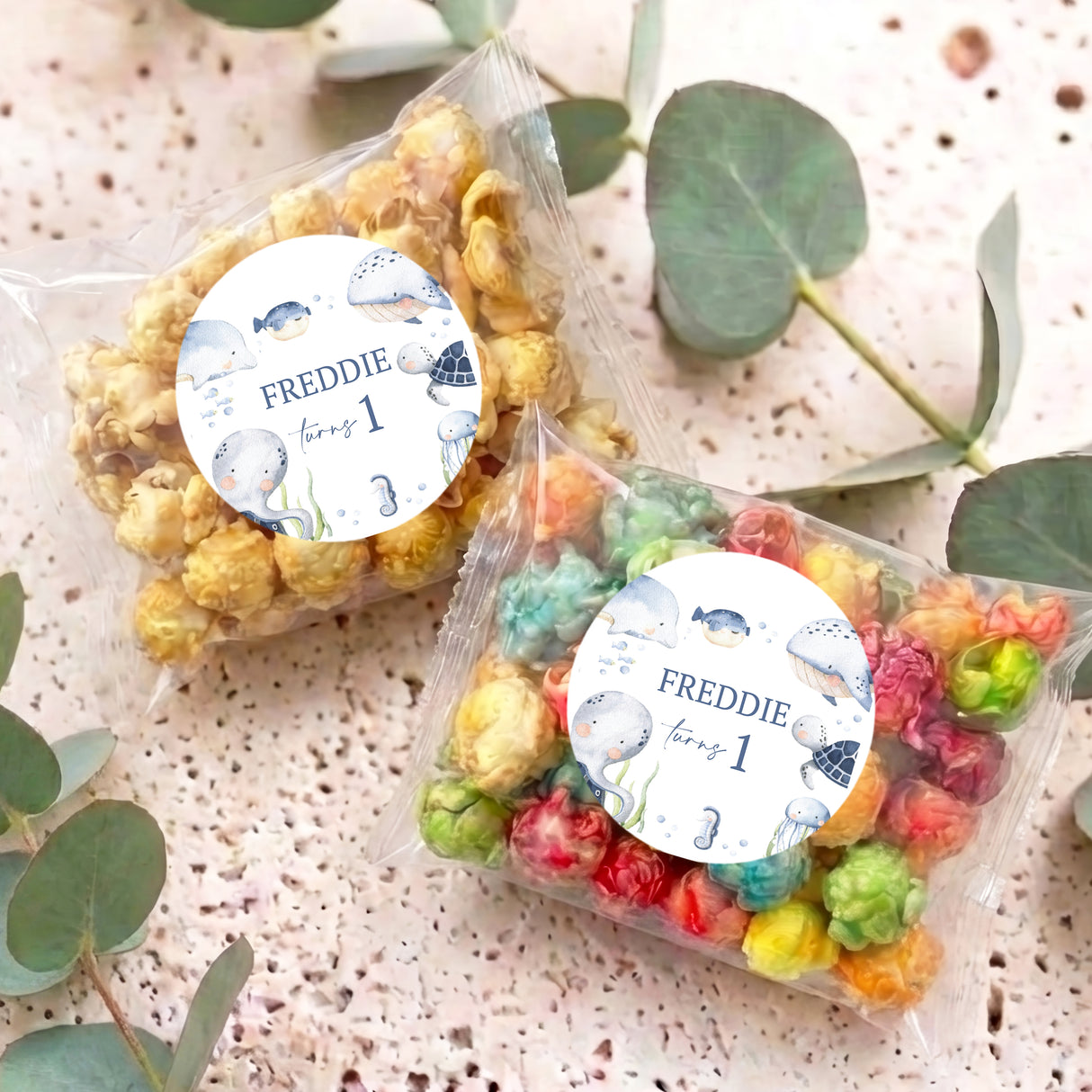 Two personalised popcorn bags with clear pouches, colorful popcorn, and round Freddie labels
