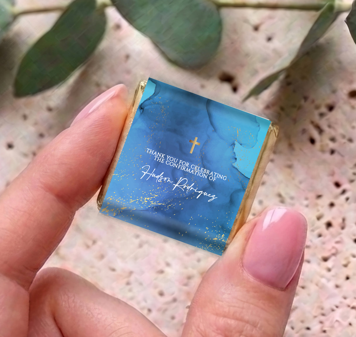 Blue mini chocolate with gold cross and confirmation message, held in hands