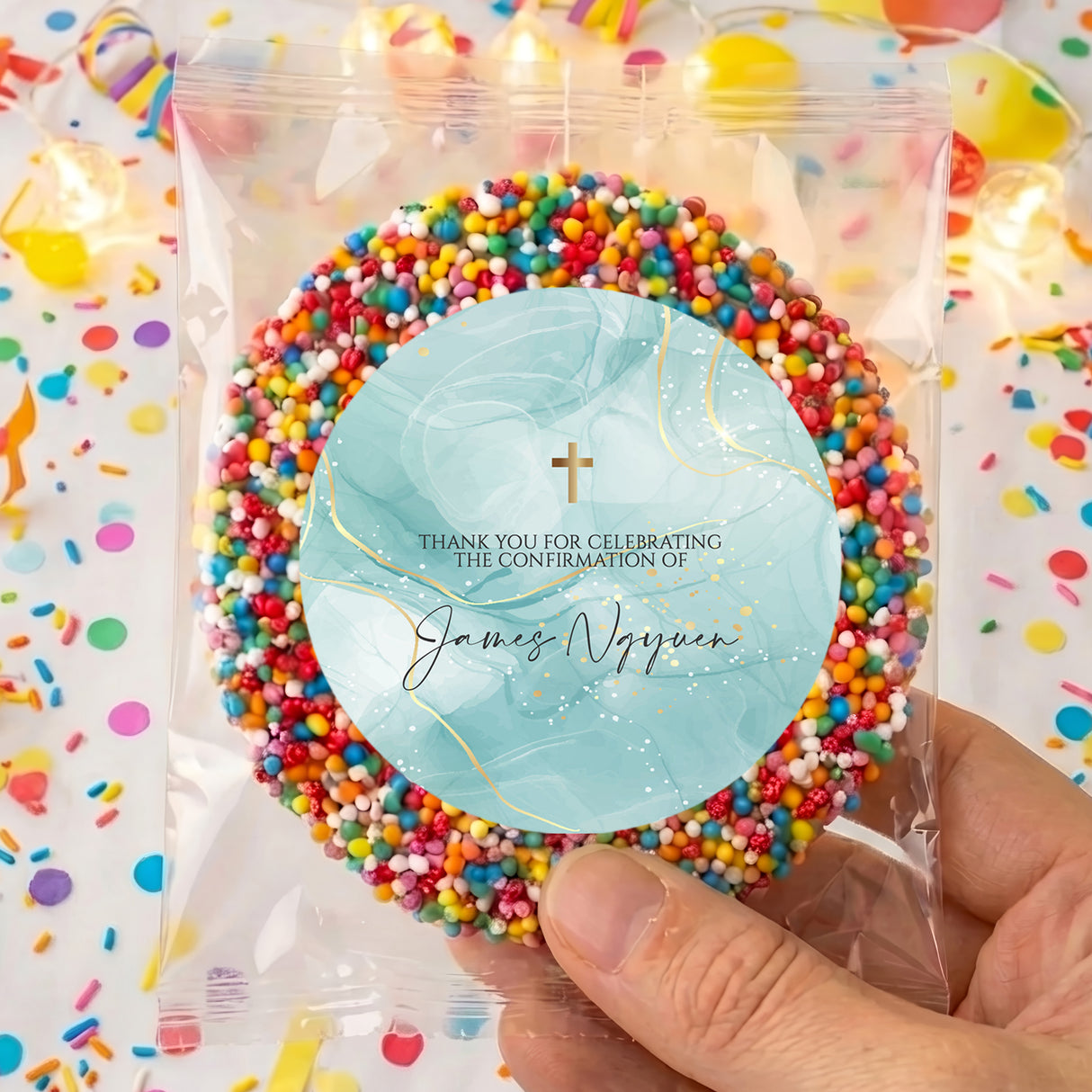 Clear bag of colorful sprinkles with round blue label, gold cross and name