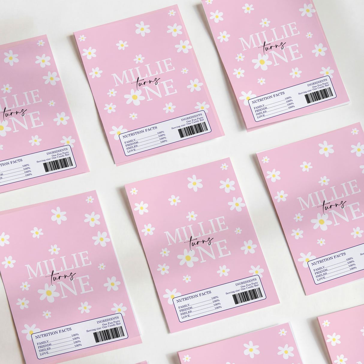 Pink DIY chocolate wrappers with white daisy pattern and 'MILLIE' text, 'turn one'.