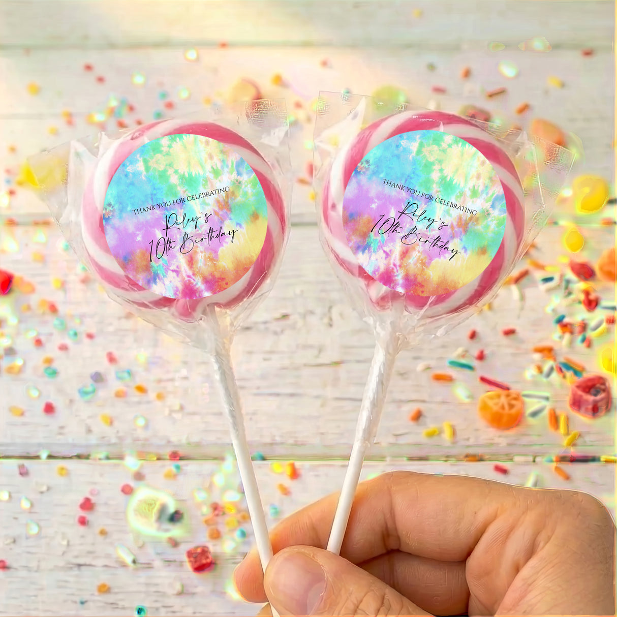 Two tie dye birthday lollipops in clear wrappers, printed message, held by hand