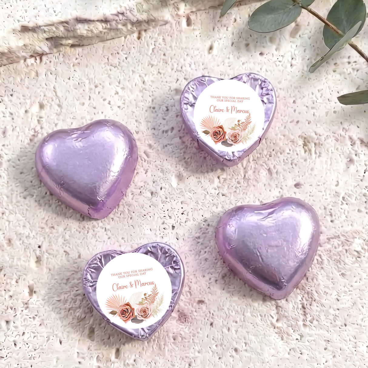 Purple foil-covered chocolate hearts with floral name labels on textured surface