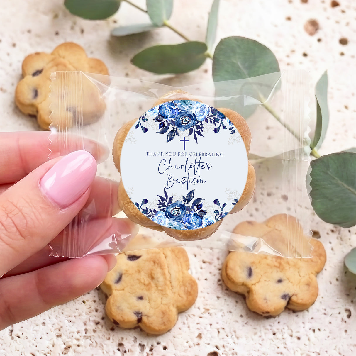 Personalised bite-size cookies in clear bag, blue floral baptism label held by hand