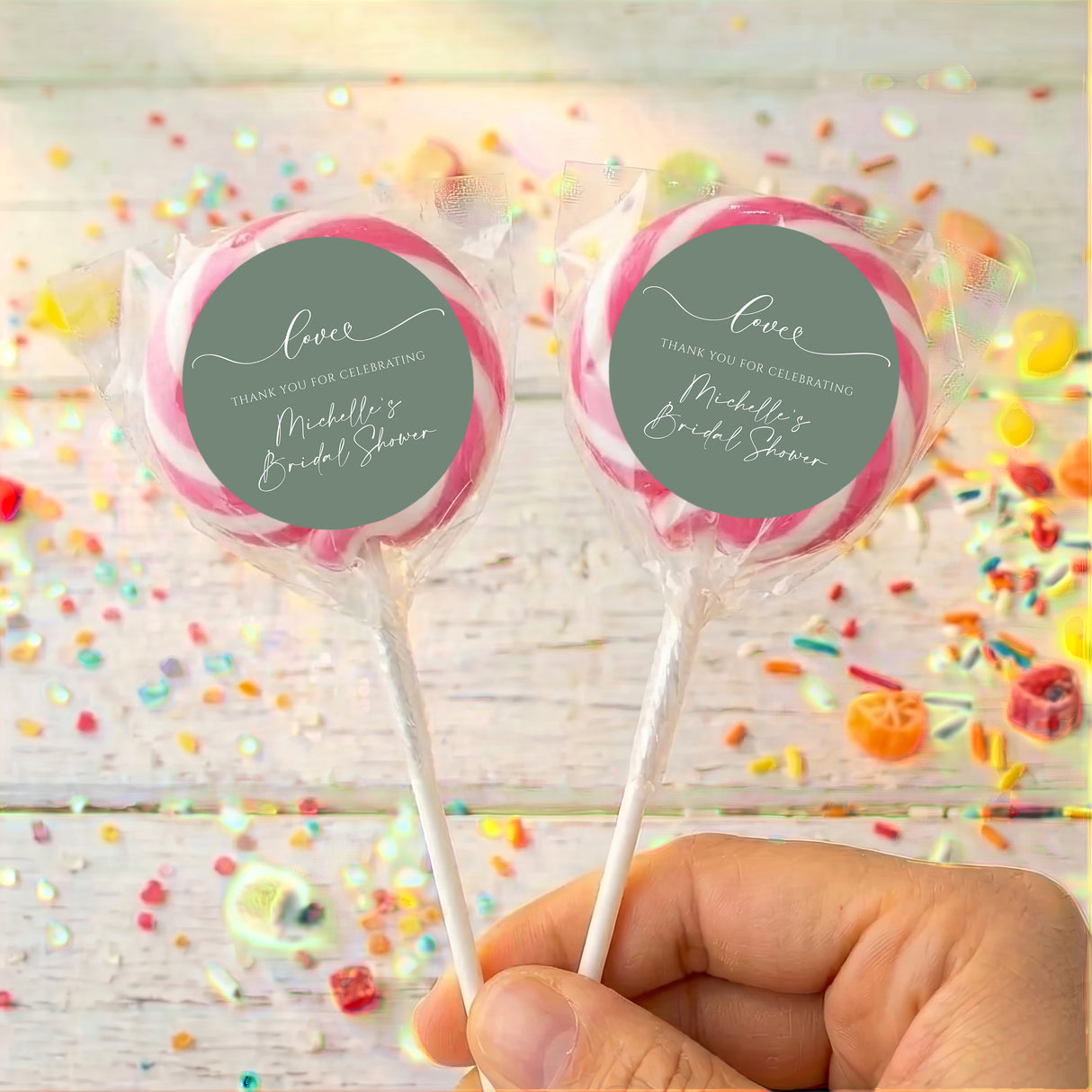 Personalised wrapped lollipops with round sage-green labels and pink ribbon accents on sticks