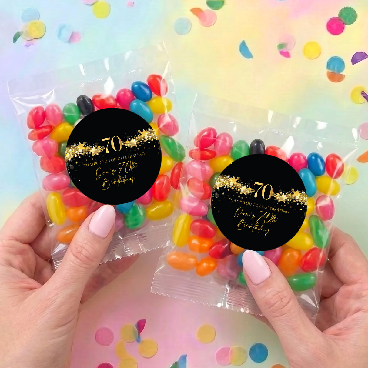 Two clear jelly bean bags held in hands, black '70th' gold-star label with jelly beans