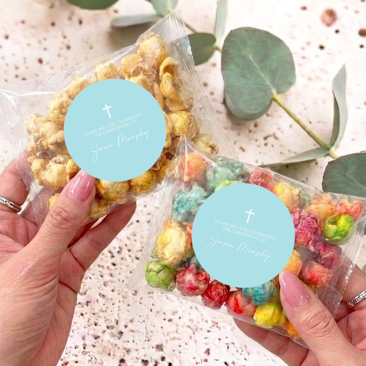 Pastel blue christening popcorn bags, clear bags with popcorn and turquoise cross labels, held