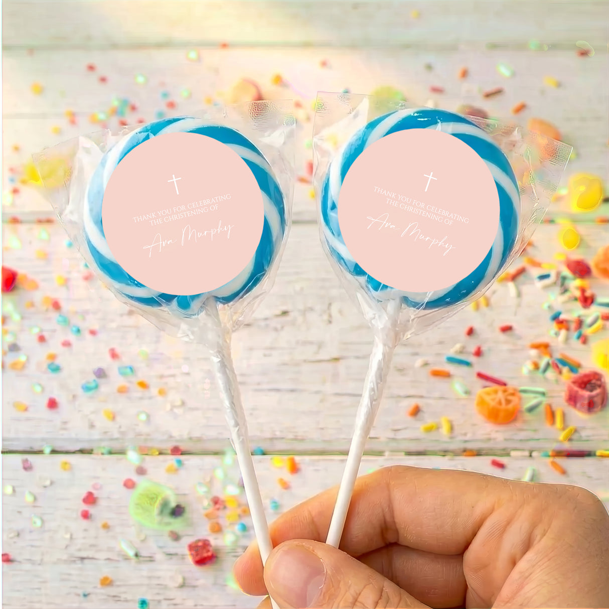Personalised cross lollipops with blue wrap, round personalised label, held in hand