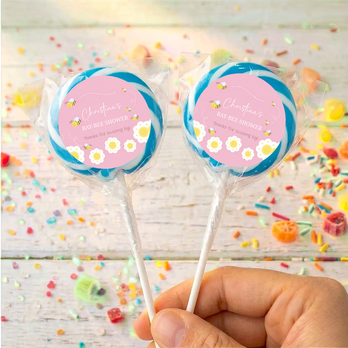 Baby shower lollipops with bee theme, two pops with blue outer wrappers and pink labels