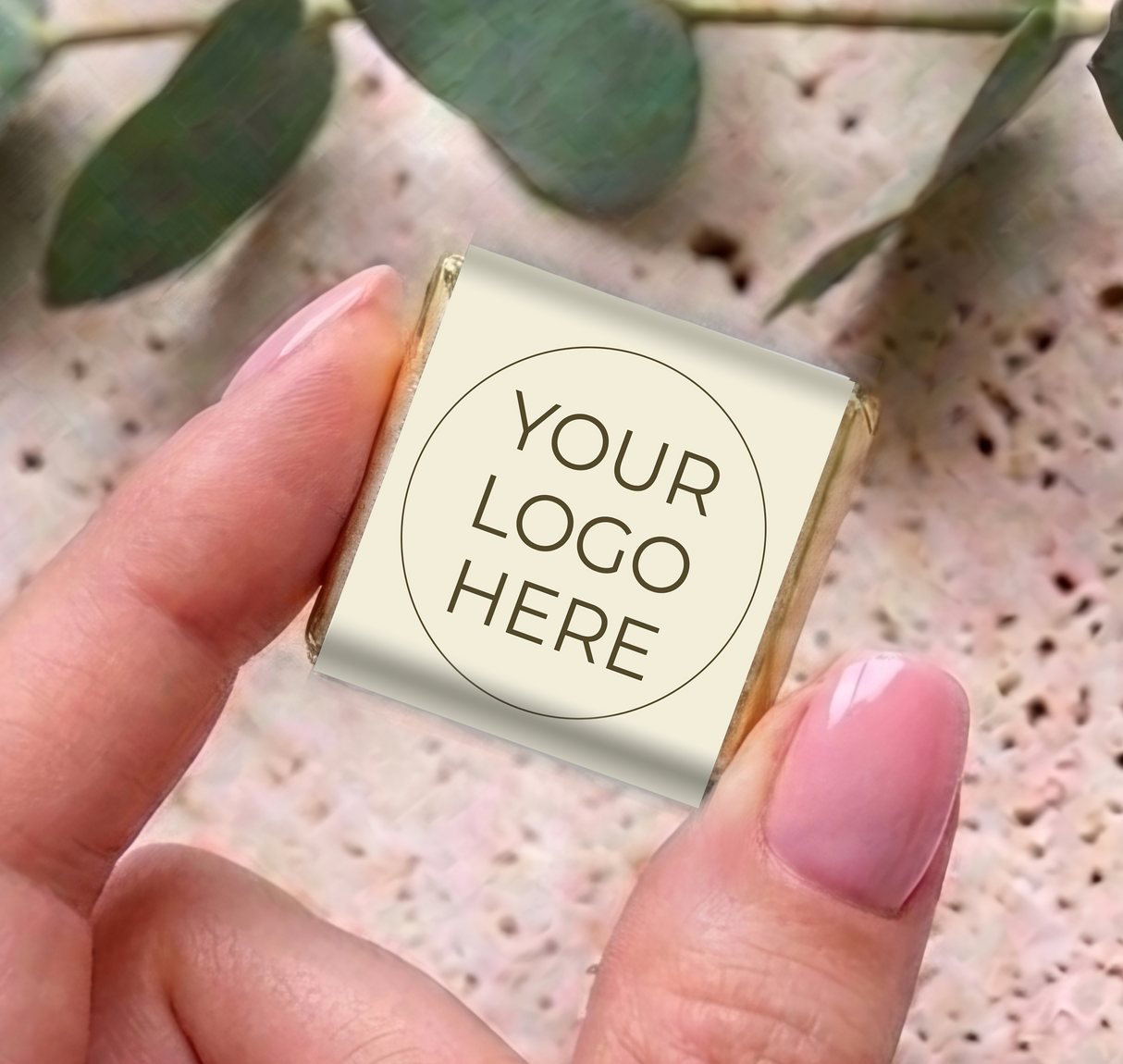 Mini personalized chocolates with cream wrapper and “YOUR LOGO HERE” label, held in hand