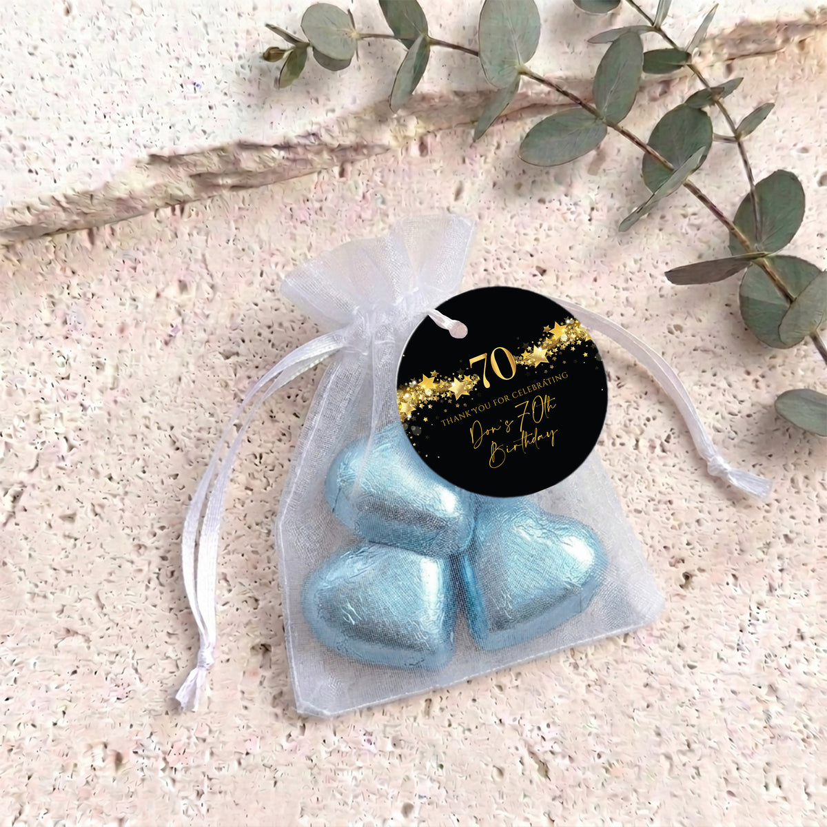 Black organza gift bag with gold stars and blue heart chocolates, round black tag