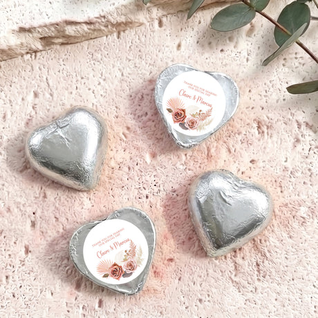 Silver foil-covered chocolate hearts with floral name labels on textured surface