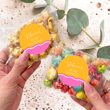 Personalised birthday popcorn bag with clear wrap and yellow name label, held in hand