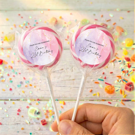Personalised birthday lollipops with pink and purple swirled wrappers, held by hand