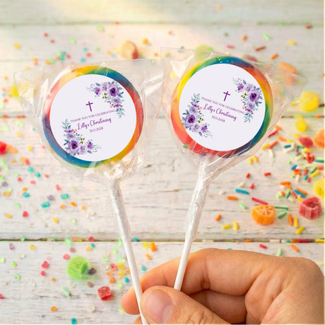 Christening lollipops with rainbow-edged floral labels on sticks, held in hand