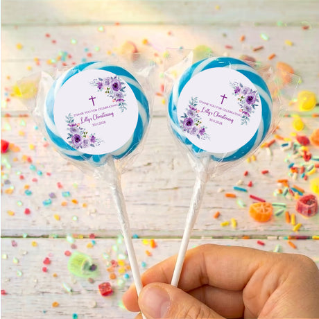 Christening lollipops with blue floral labels on sticks, held in hand