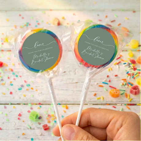 Personalised wrapped lollipops with round sage-green labels and multicolor ribbon edges on sticks