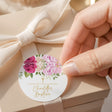 Round christening label with pink and white roses, green leaves, cross, and gold text