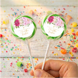 Two Christening lollipops in clear wrappers, held by a hand; green rose floral design