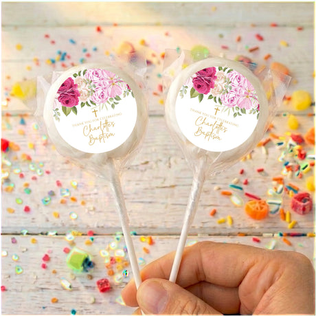 Two pink rose baptism lollipops with floral labels on clear wrappers, on sticks