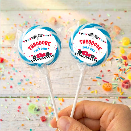 Personalised race car lollipops with “THEODORE” labels, blue ribbons, two on sticks