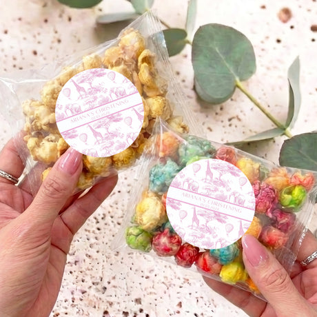 Pink safari-themed popcorn bag set with round white personalised labels, held by hands