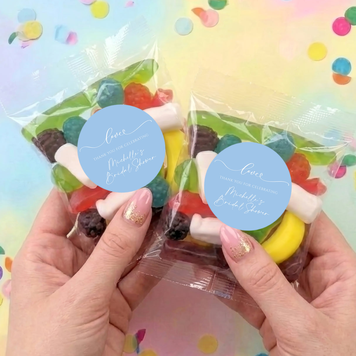 Two personalised lolly bags with mixed sweets and blue round thank-you labels, held in hands