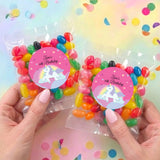 Two personalised 6th birthday unicorn jelly bean bags, hands holding pink rainbow labels