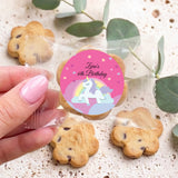Hand holding choc chip cookie with pink unicorn birthday sticker and clear wrapper