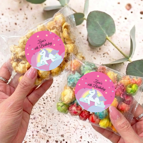 Personalised unicorn birthday popcorn bag with pink label, held in hands