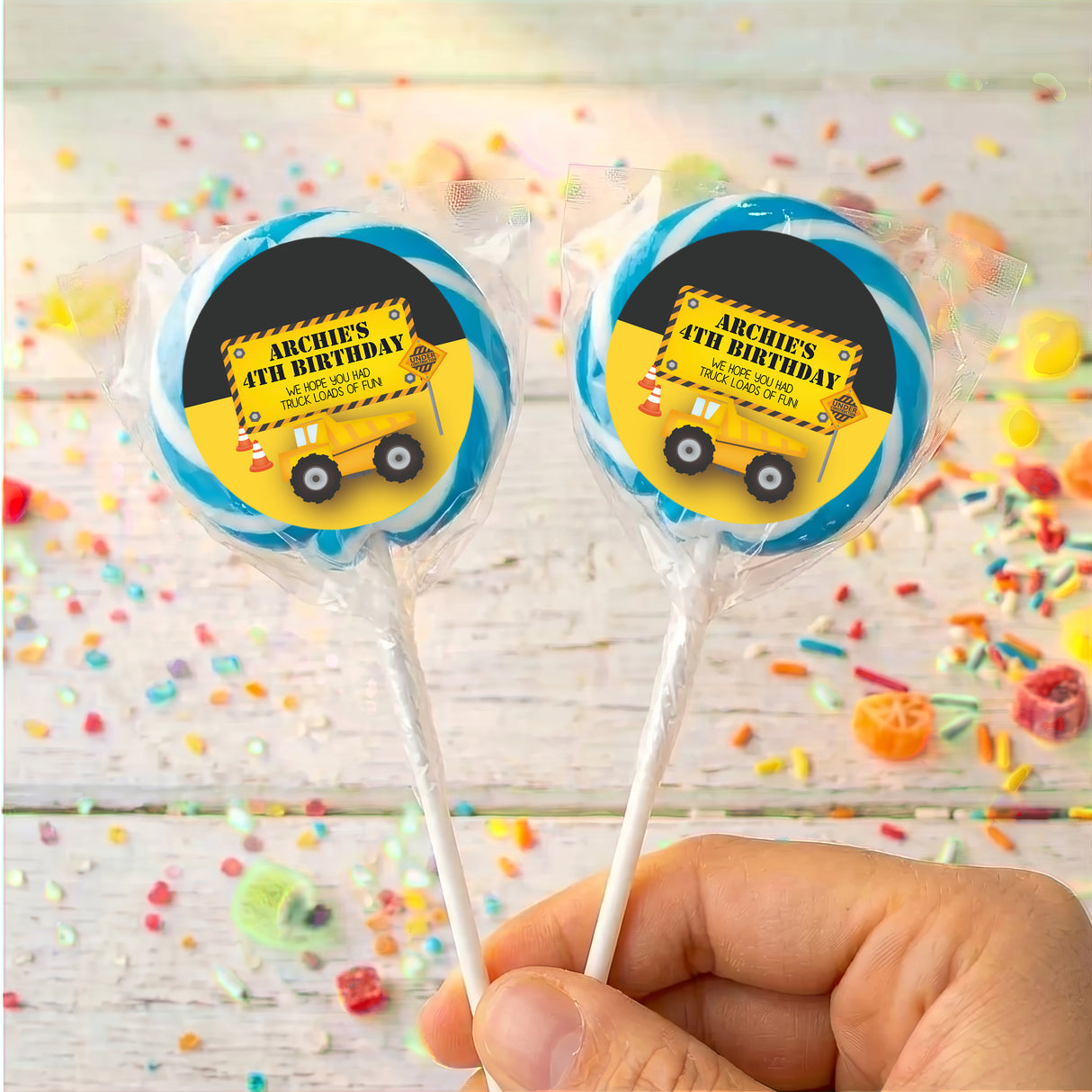Personalised birthday lollipops with yellow truck labels in blue border, held in hand