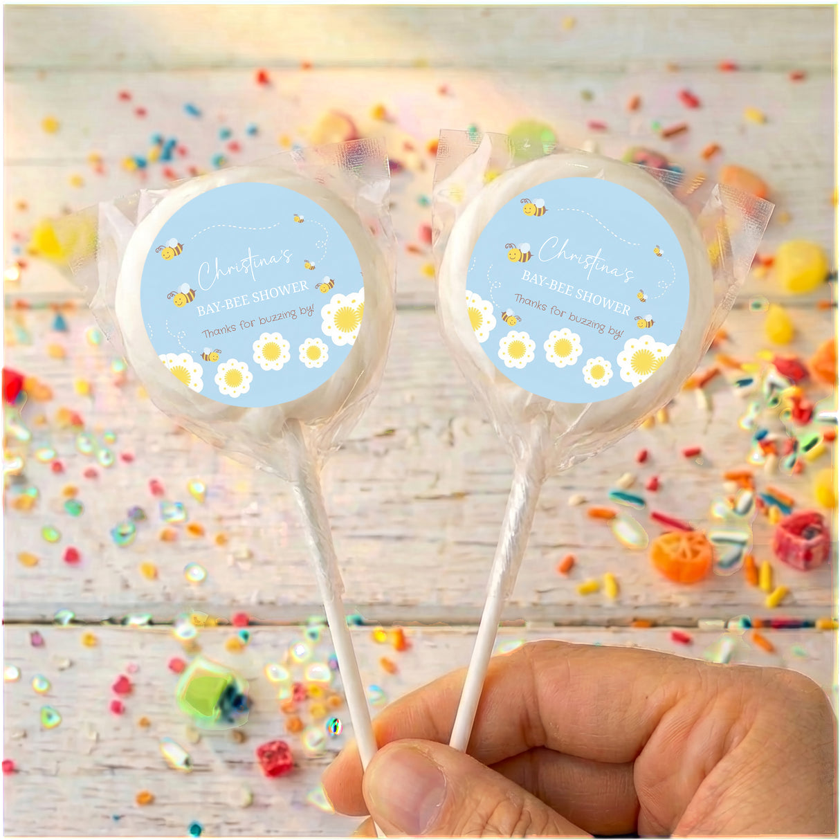 Personalised blue bee baby shower lollipops, two clear-wrapped sticks with round labels