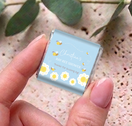 Hand holding a blue mini personalized chocolate box with “Bay-Bee Shower” bee theme