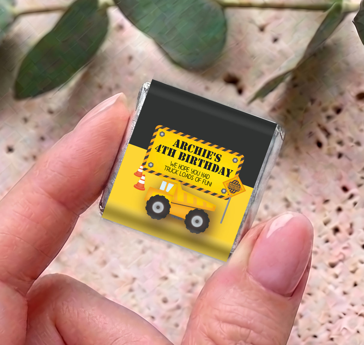 Personalised mini chocolate bar in foil with yellow truck birthday wrapper, held between fingers