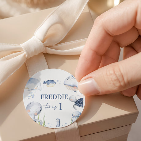 Round sea-themed label with whales, bubbles, and text 'FREDDIE turning 1'