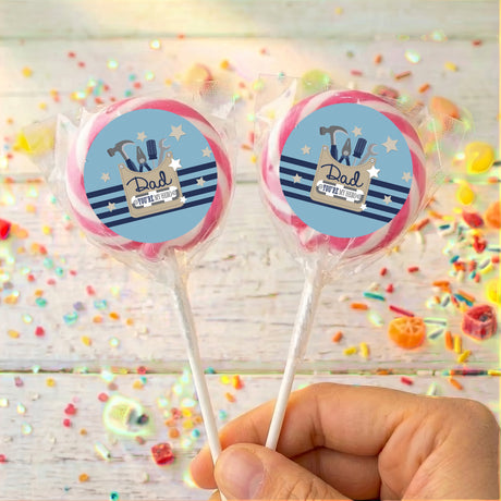 Personalised Father’s Day lollipops with blue “Dad” tools logos, pink-rimmed, held in hand