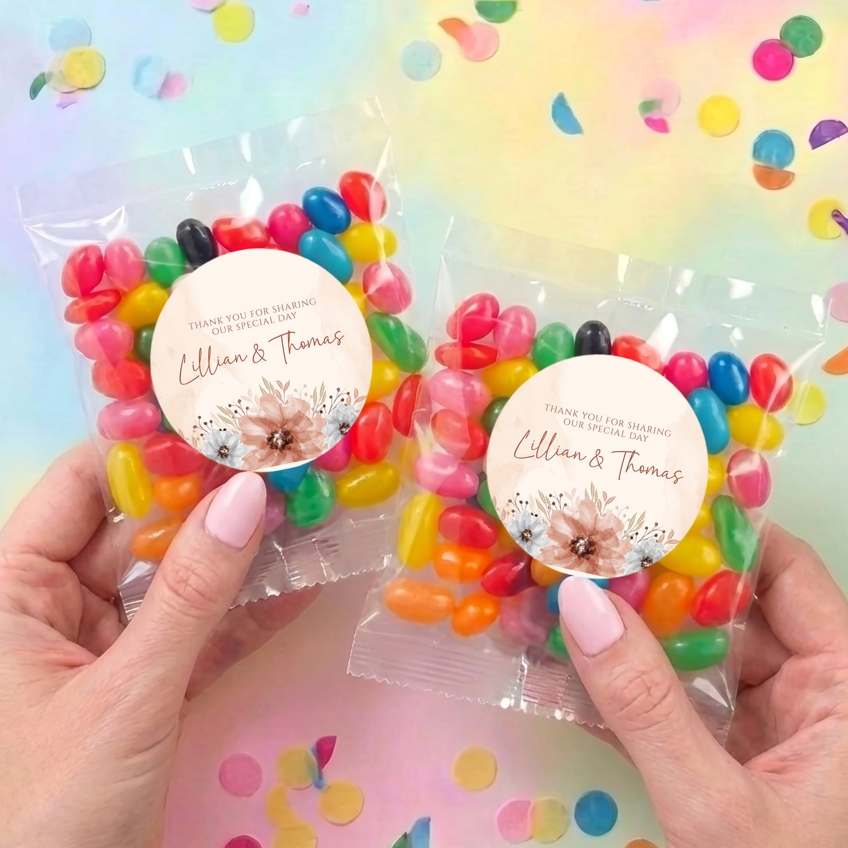 Two jelly bean favour bags in hands, each with round floral thank-you label and colorful sweets
