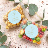 Two personalised popcorn bags with cross logo light blue labels and clear bags of colorful popcorn