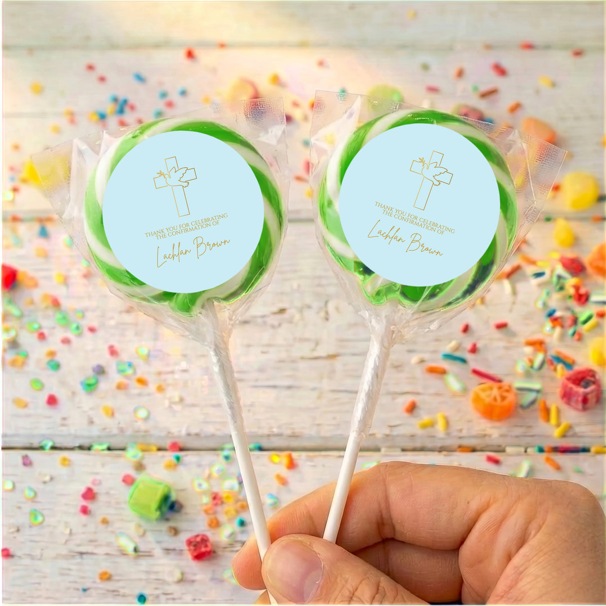 Personalised lollipops with green ribbon trim, clear wrappers, round blue labels with cross icon